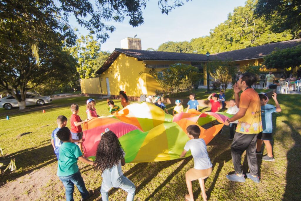 Group of children playing with a colorful parachute outside during a sunny day party.